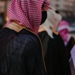 Close-up of an adult wearing traditional Saudi attire, featuring a red and white kaffiyeh and black mask.